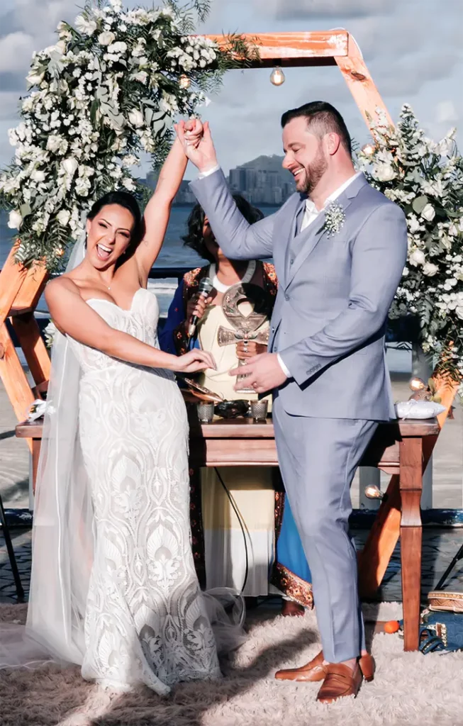 Lorene Batan no dia do próprio casamento, de mãos dadas com o marido sob um arco de flores